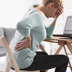 Woman working on a laptop and having headache and back, hip, spine pain.