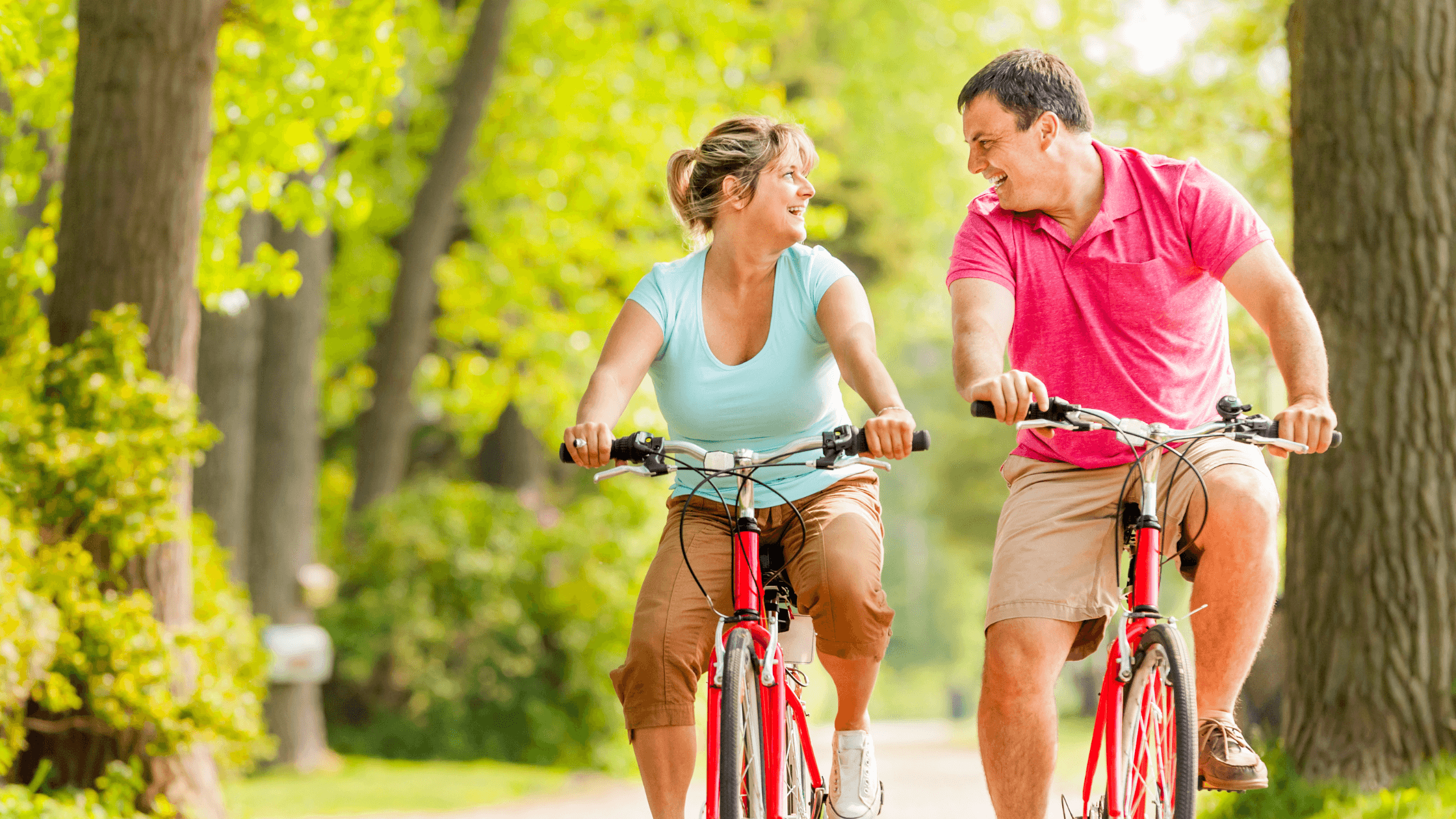 A smiling couple enjoys a leisurely bike ride through a sun-dappled park, illustrating an active lifestyle made possible by effective back pain management.
