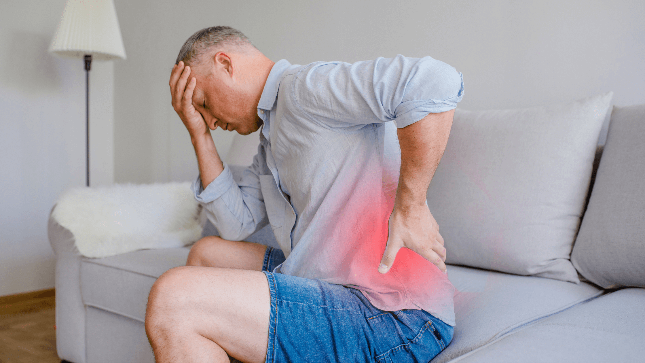 A man sits on a sofa, holding his lower back with a red glow highlighting the painful area, representing the discomfort from a herniated disc that an epidural injection aims to relieve.