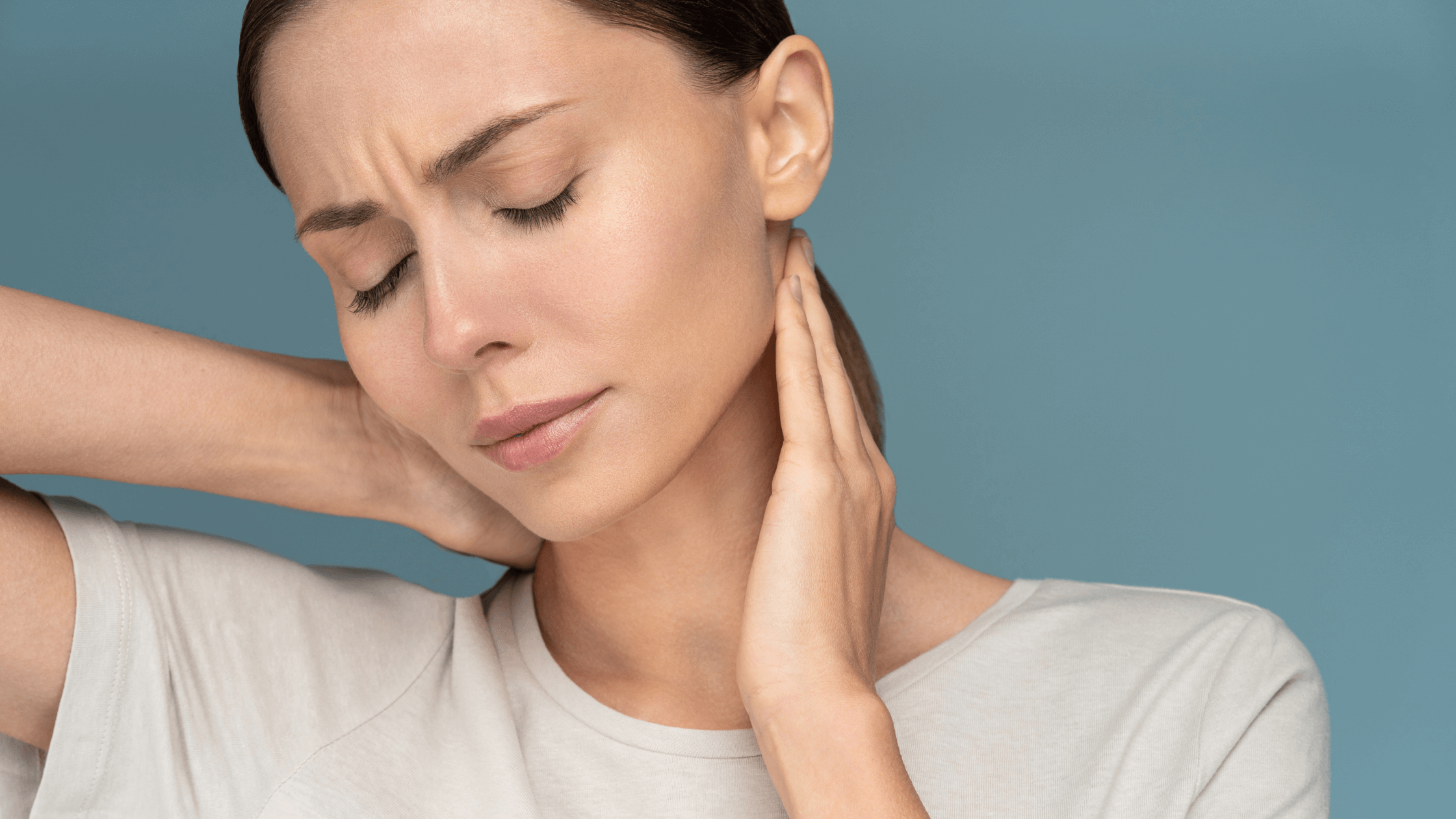 A woman in a white shirt holding her neck with a concerned expression, illustrating the frustration of chronic pain that persists despite resting.