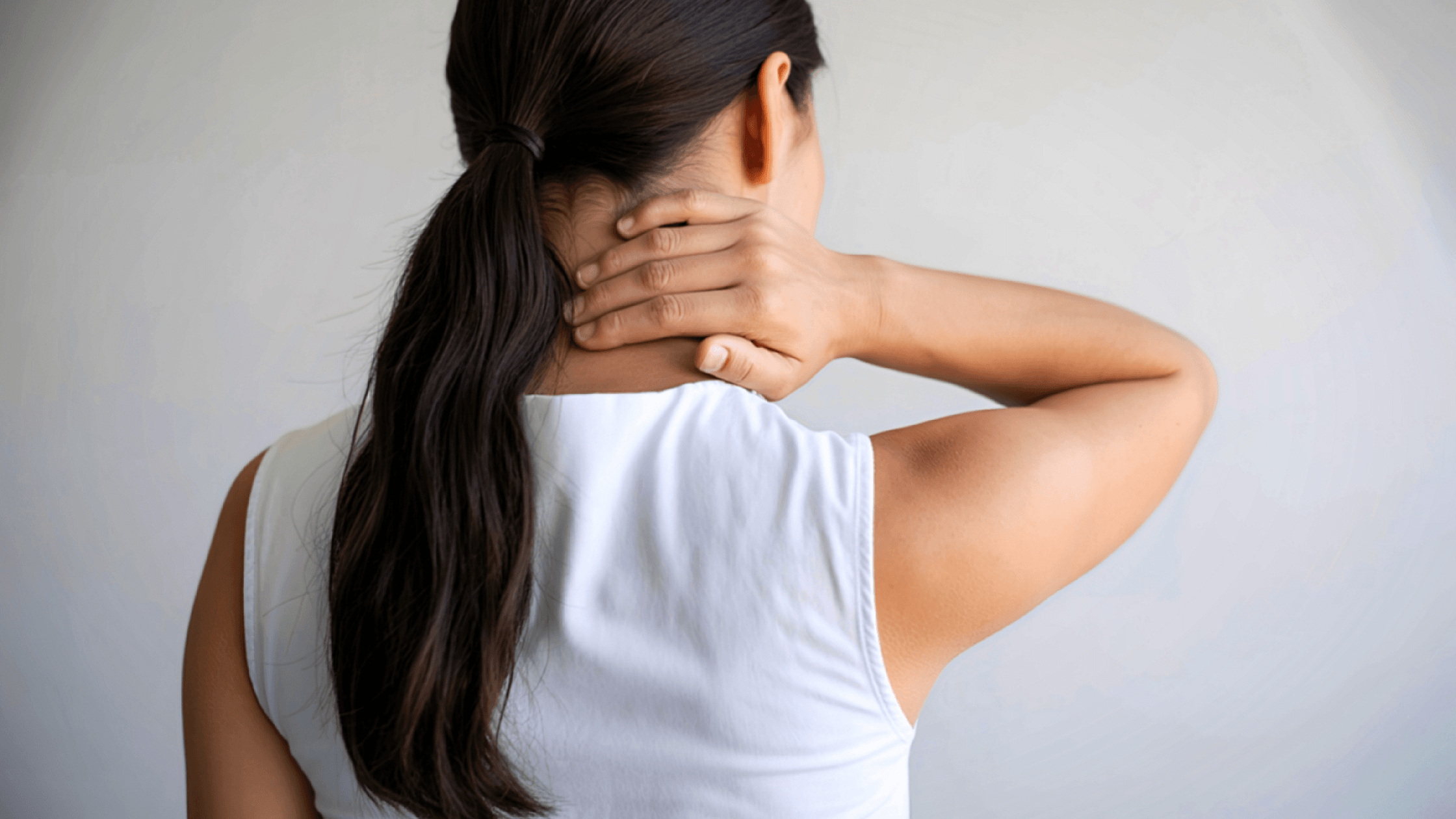 Rear view of a woman in a white sleeveless top holding the back of her neck in pain, highlighting the cervical spine area.